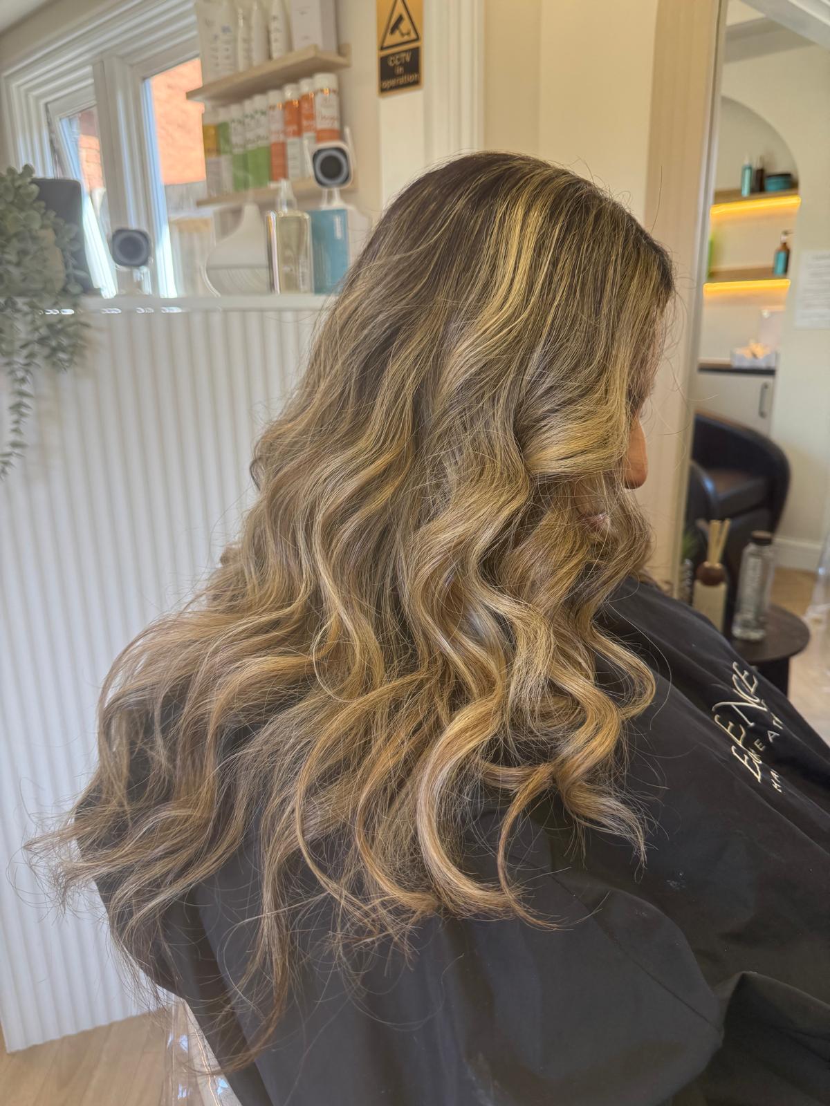 Sun-kissed blonde balayage on long, loose curls at Essence in Luton